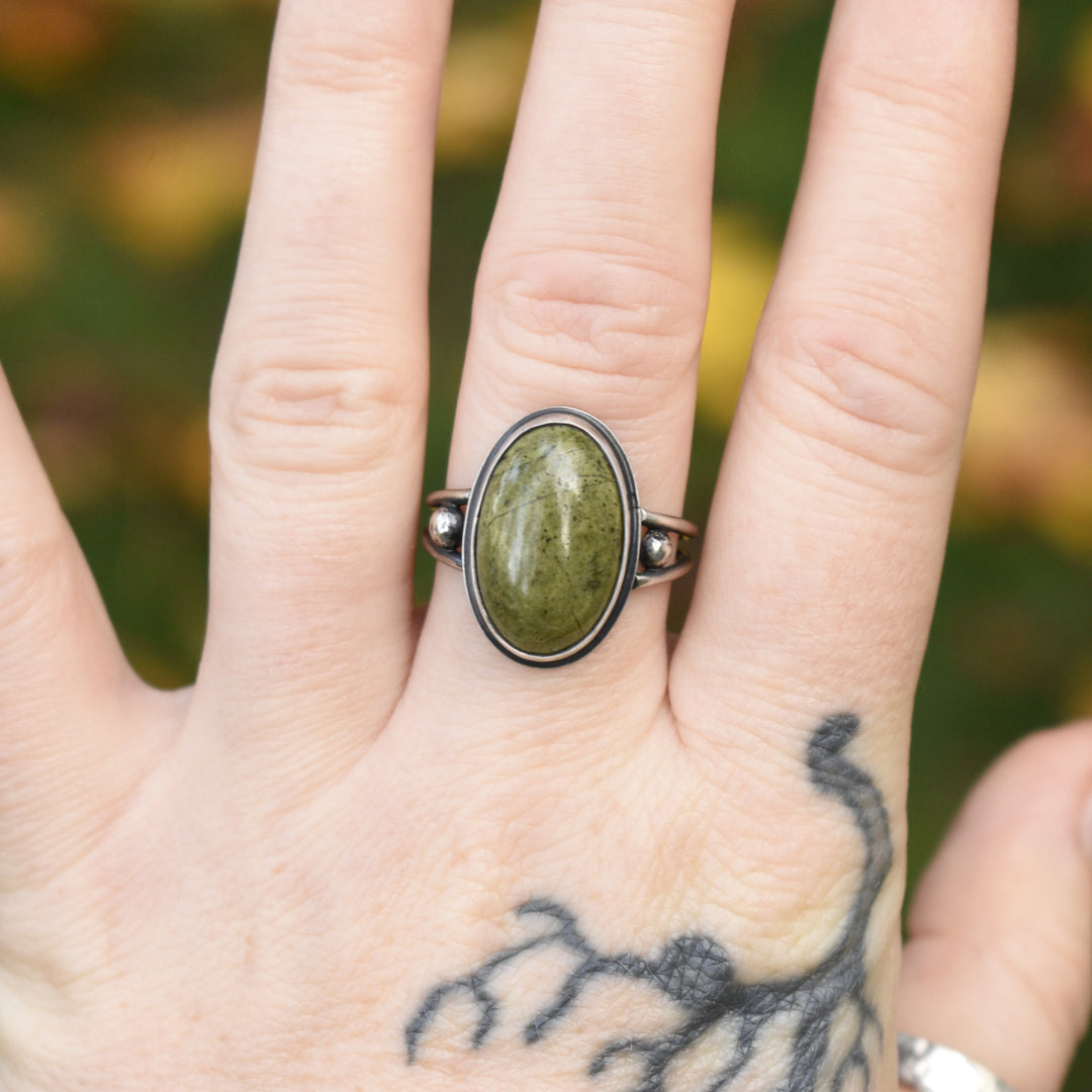 Hand wearing a ring with a green stone against a blurred natural background