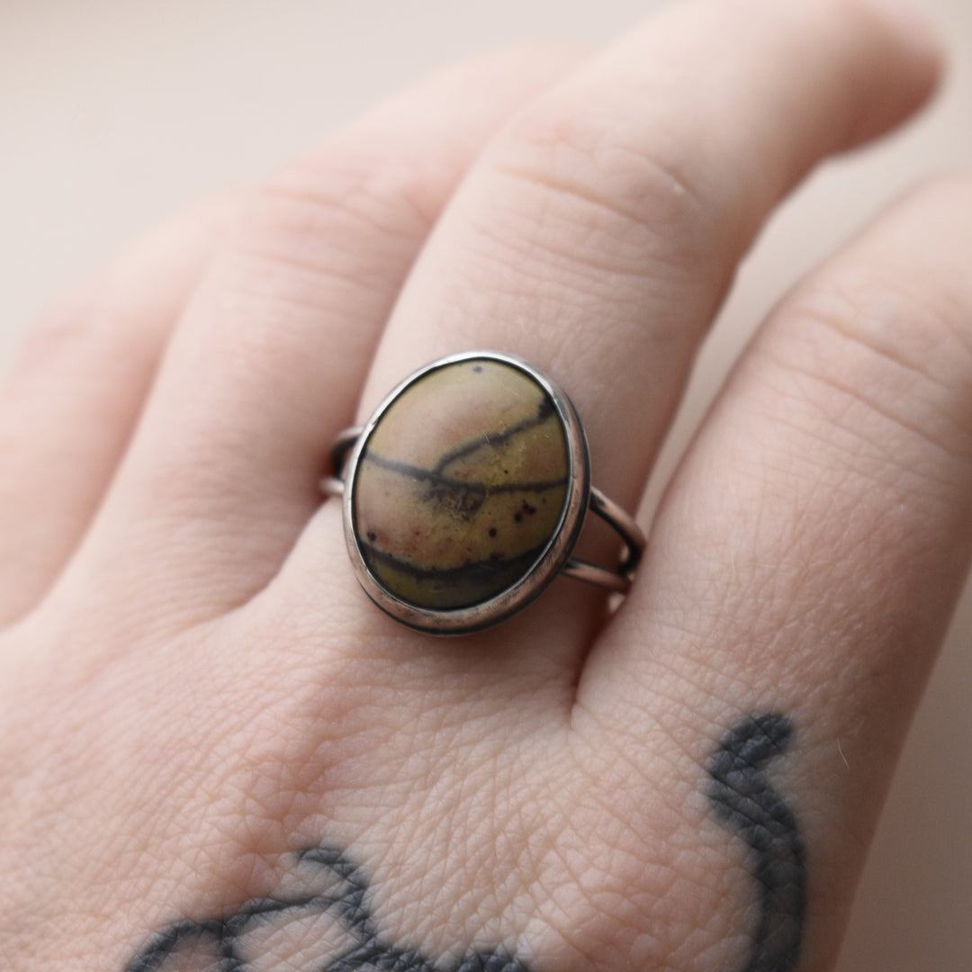 Ring with a Banana Jasper stone on a person's finger with tattoos.