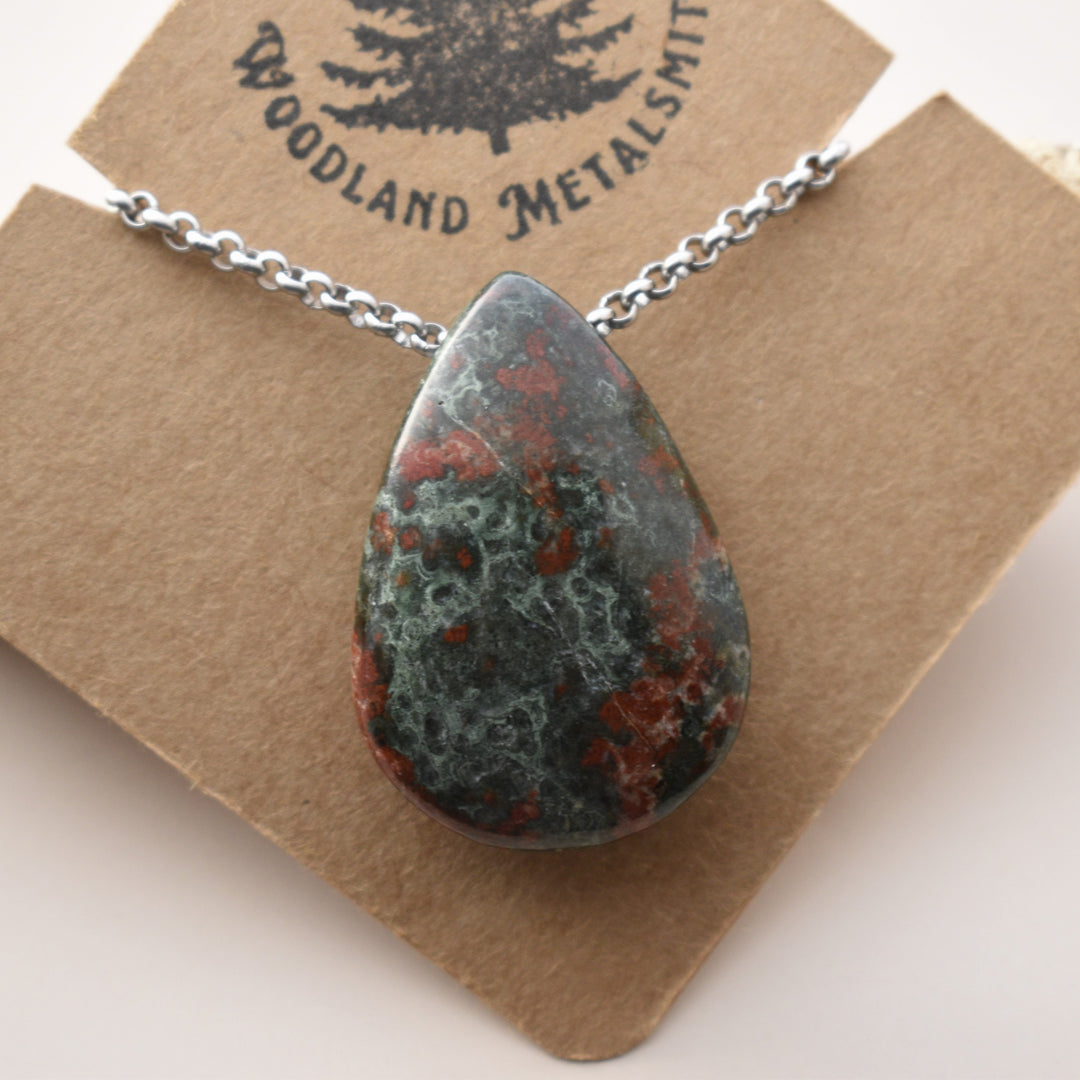 Teardrop-shaped stone pendant on a chain with 'Woodland Metalsmith' branding on a brown card.