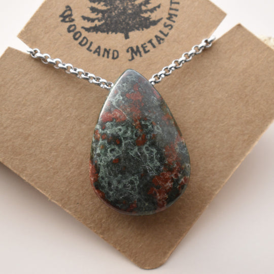 Teardrop-shaped stone pendant on a chain with 'Woodland Metalsmith' branding on a brown card.