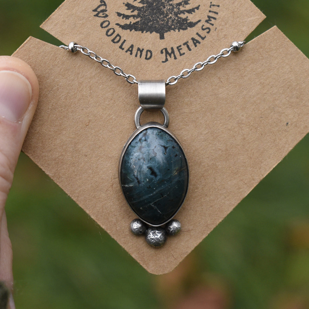 Necklace with a blue stone pendant on a 'Woodland Metalsmith' card.