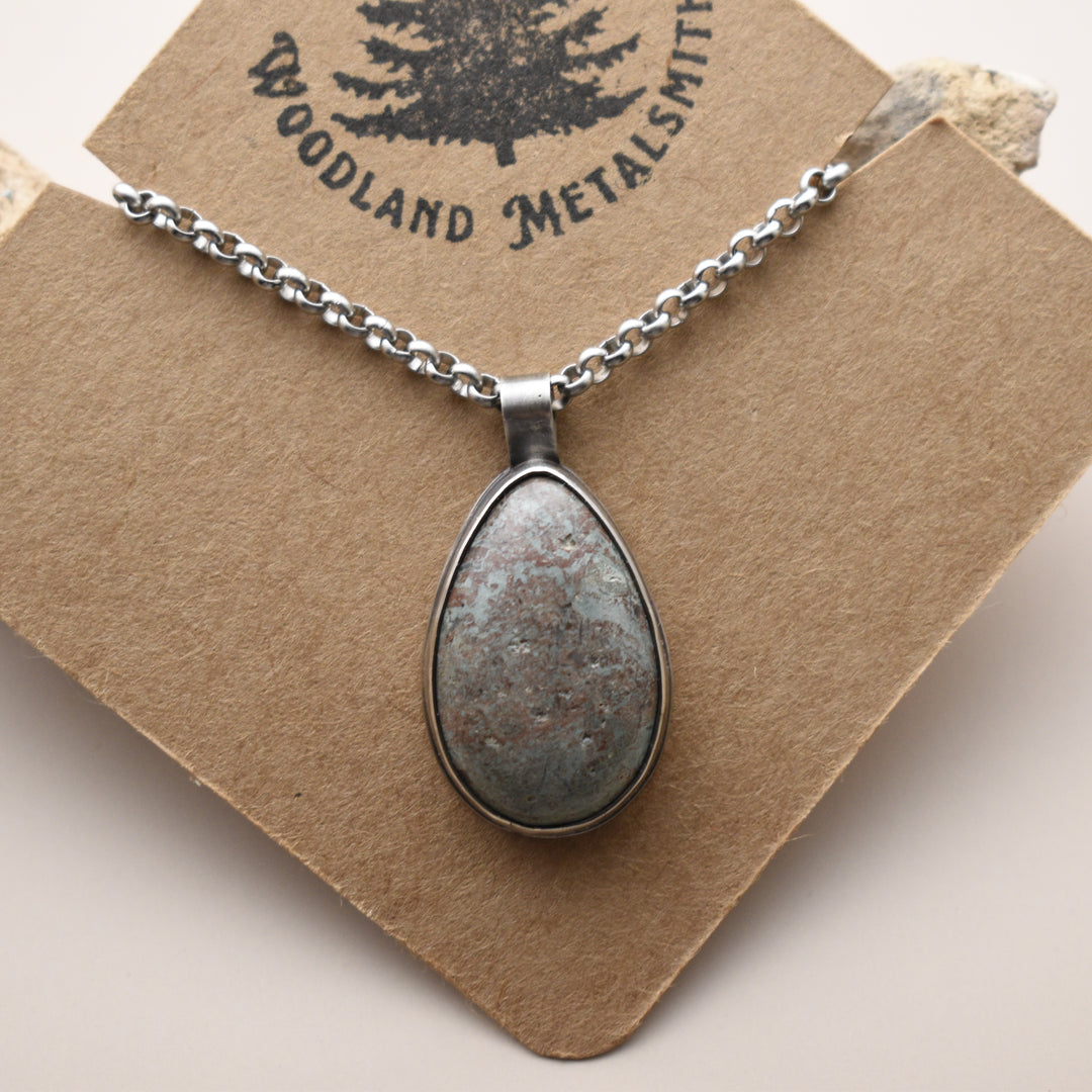 Blue Stone necklace with a teardrop-shaped pendant on a 'Woodland Metalsmith' branded card.