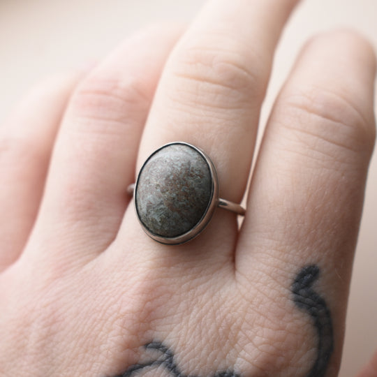 Ring with a blue stone on a person's finger against a neutral background