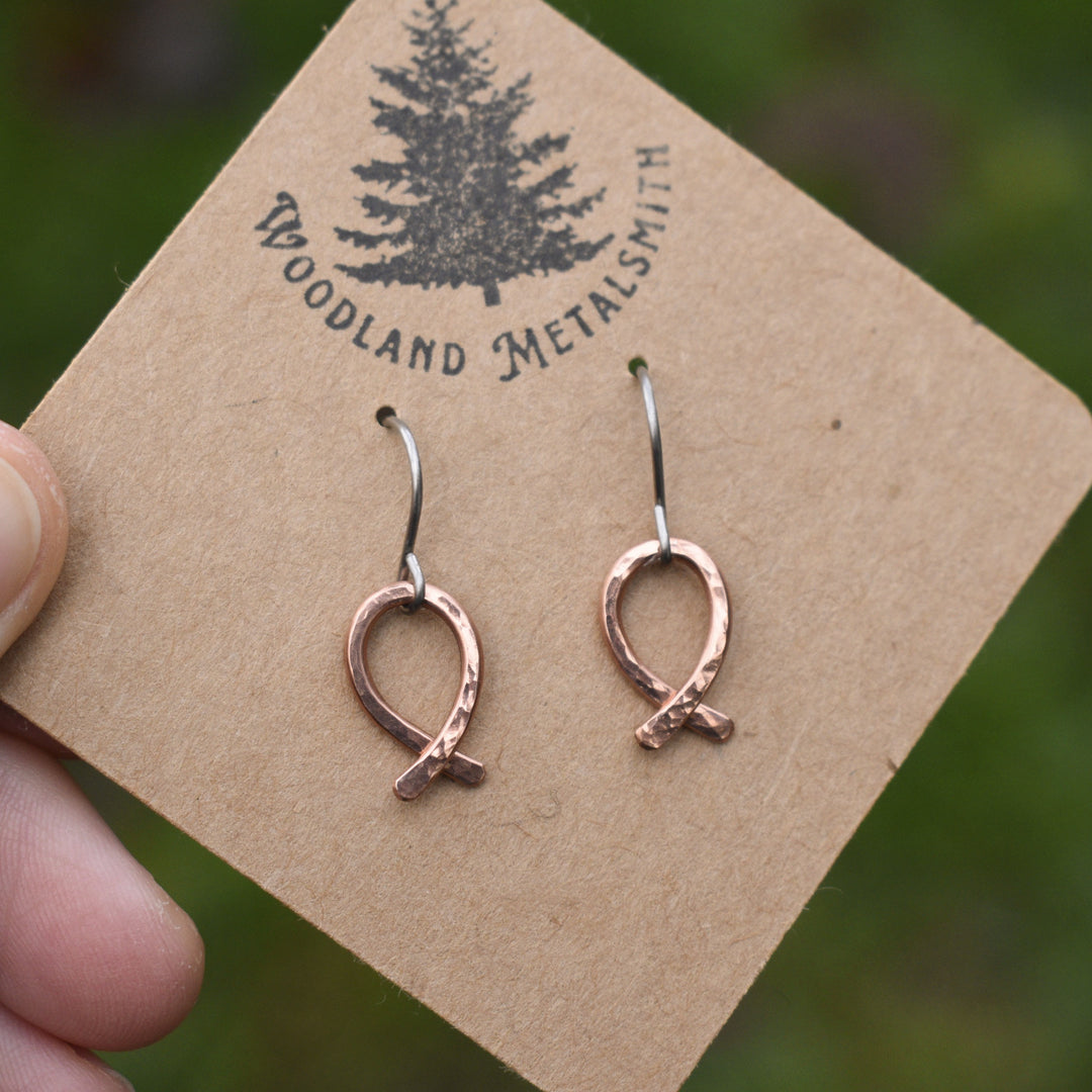 Copper fish-shaped earrings on a 'Woodland Metalsmith' branded card.