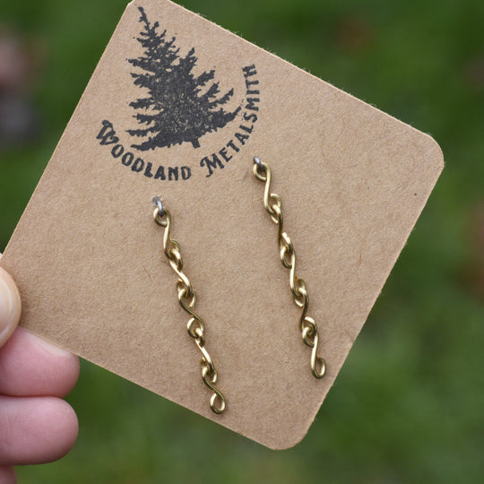 Gold chain earrings on a 'Woodland Metalsmith' branded card against a blurred green background.