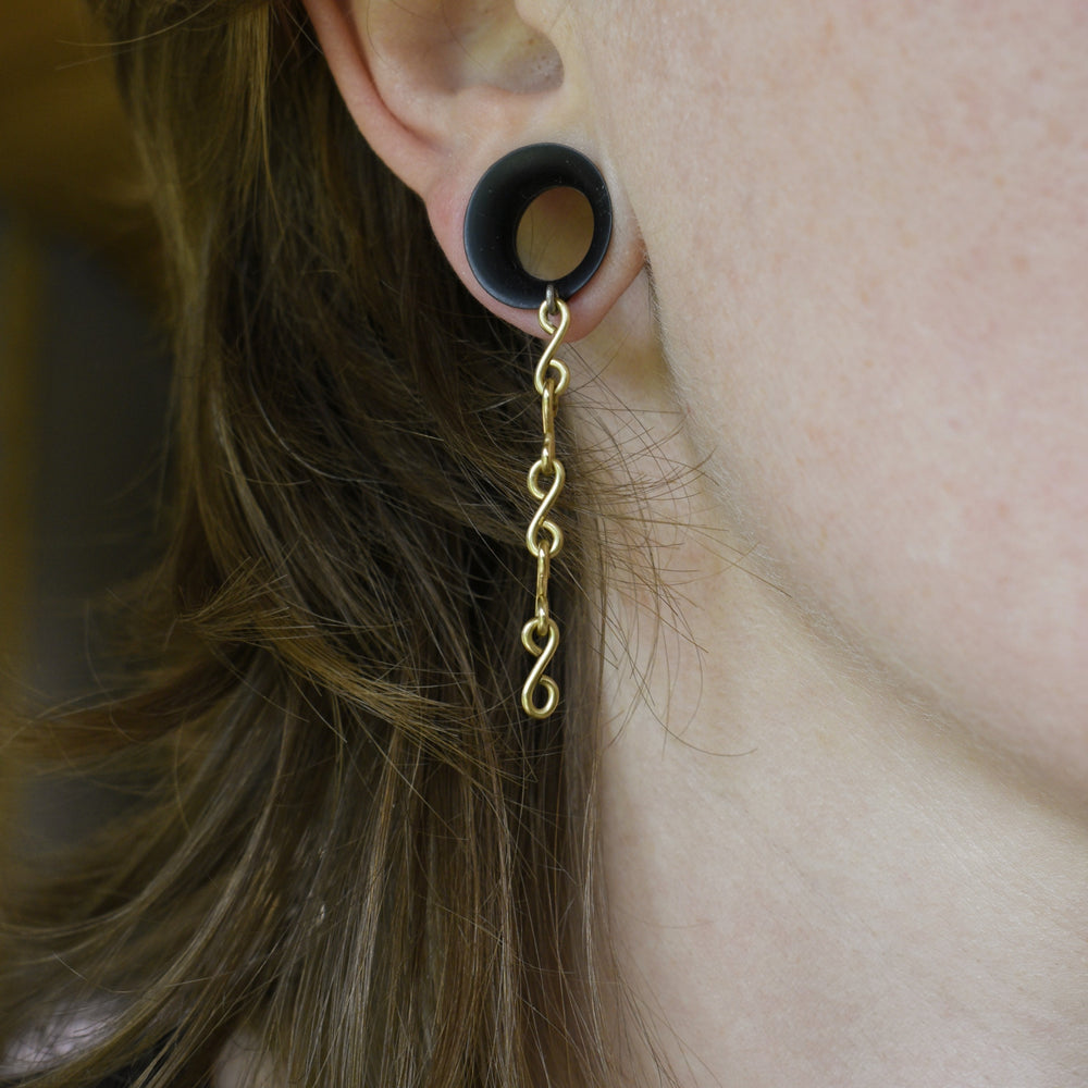 Gold spiral earring worn in an ear with a blurred background