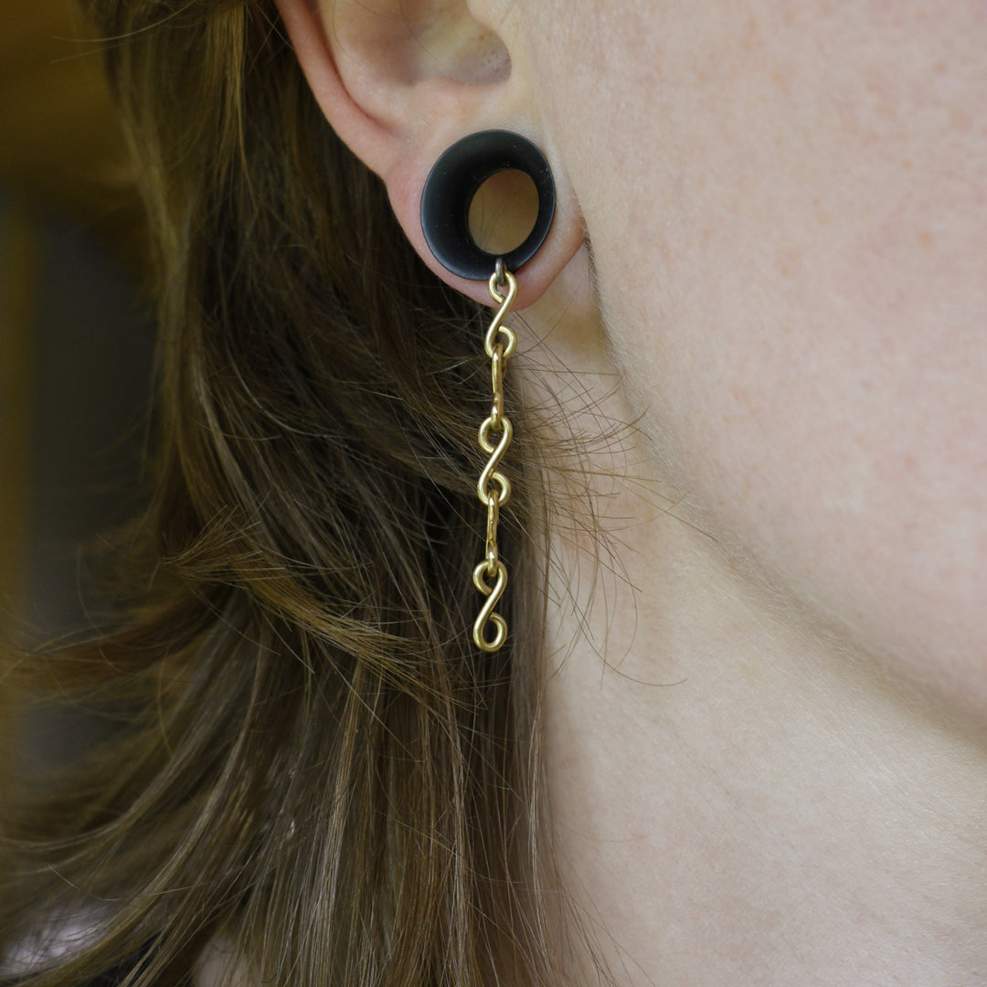 Gold spiral earring worn in an ear with a blurred background