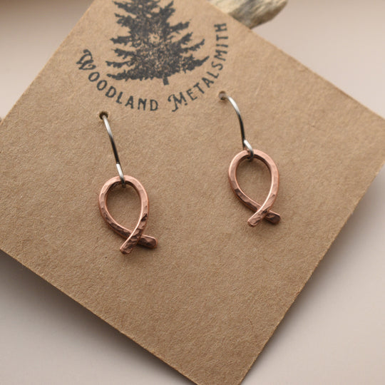 Copper fish-shaped earrings on a 'Woodland Metalsmith' branded card.