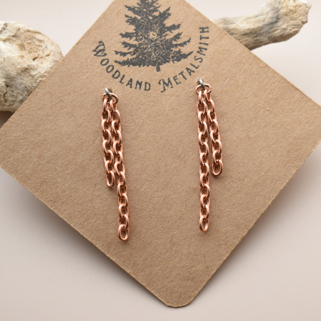 Rose gold chain earrings on a 'Woodland Metalsmith' branded card with natural elements in the background.
