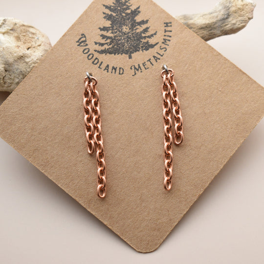 Rose gold chain earrings on a 'Woodland Metalsmith' branded card with natural elements in the background.