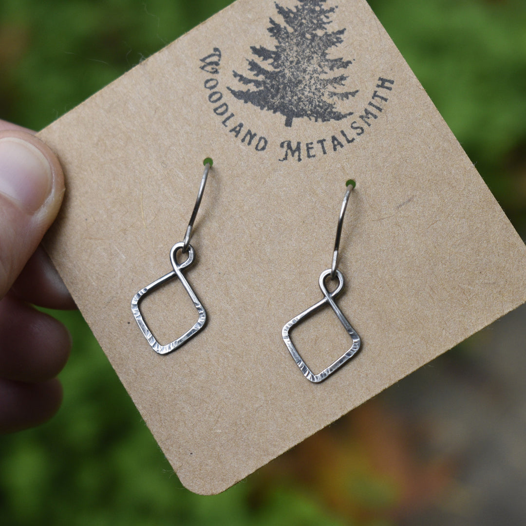 Silver earrings on a 'Woodland Metalsmith' branded card with a blurred natural background