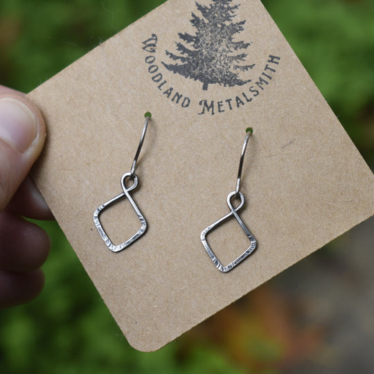 Silver earrings on a 'Woodland Metalsmith' branded card with a blurred natural background