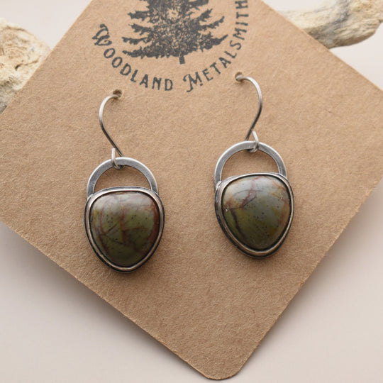 Pair of earrings with green stones on a 'Woodland Metalsmith' card.