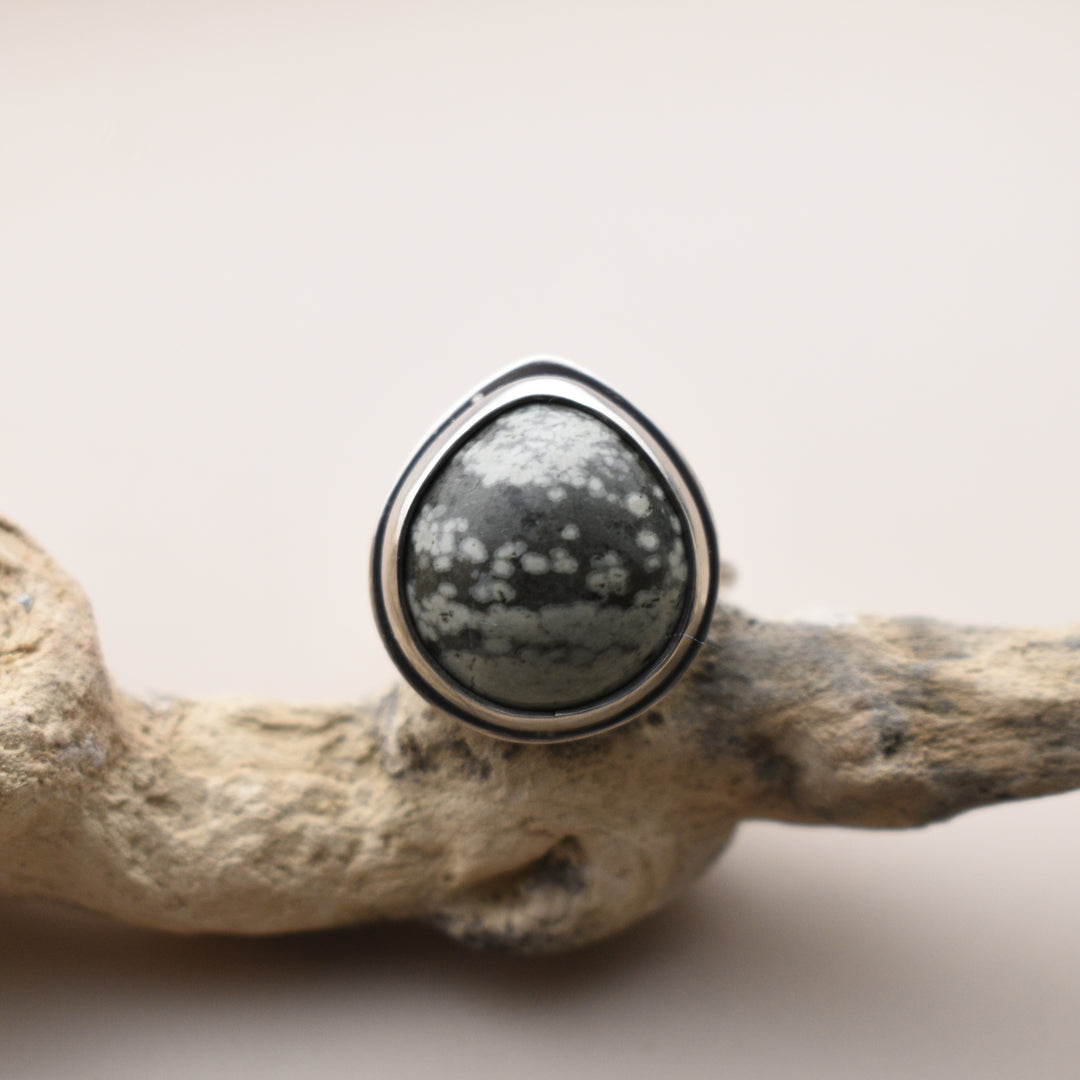 Silver ring with a green and white speckled stone on a natural wood background