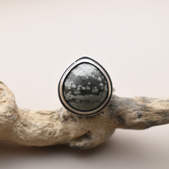 Silver ring with a green and white speckled stone on a natural wood background
