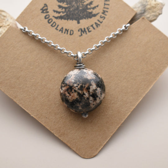 Necklace with a round stone pendant on a brown card with 'Woodland Metalsmith' branding.