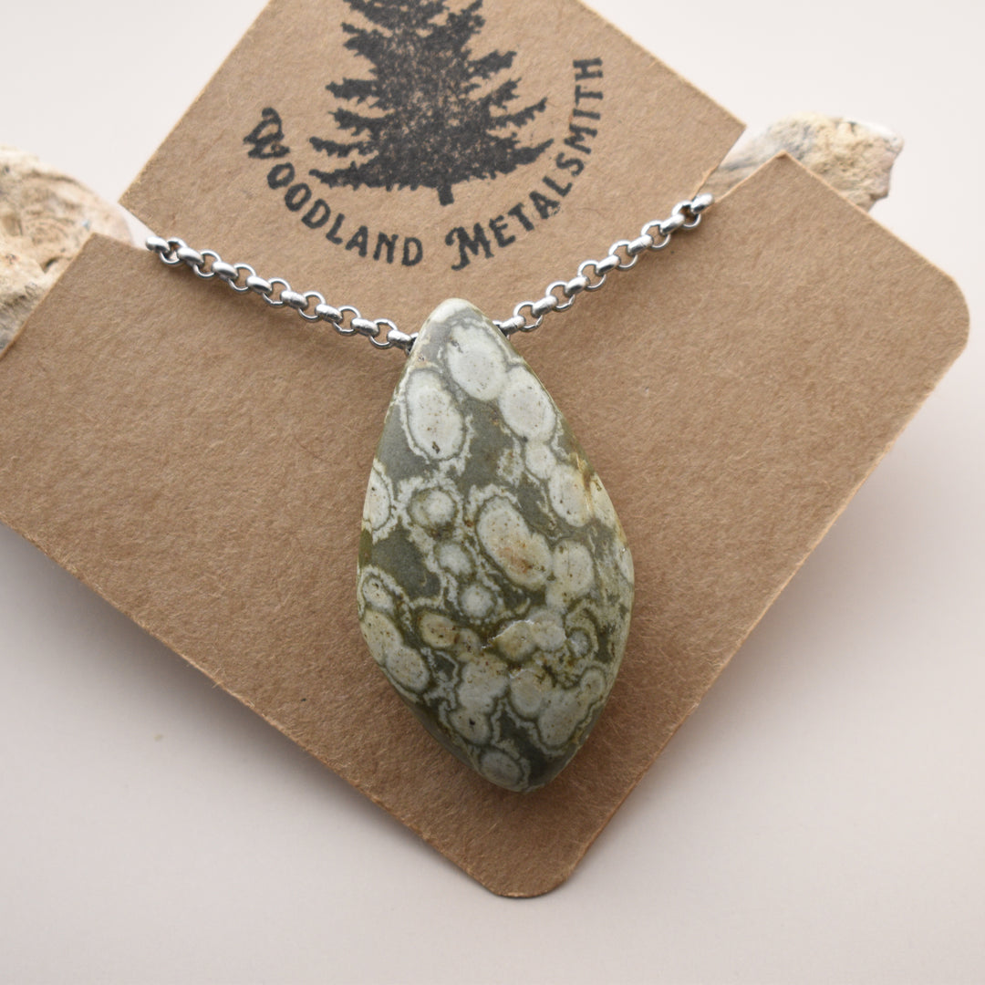 Necklace with a teardrop-shaped green stone pendant on a 'Woodland Metalsmith' branded card.