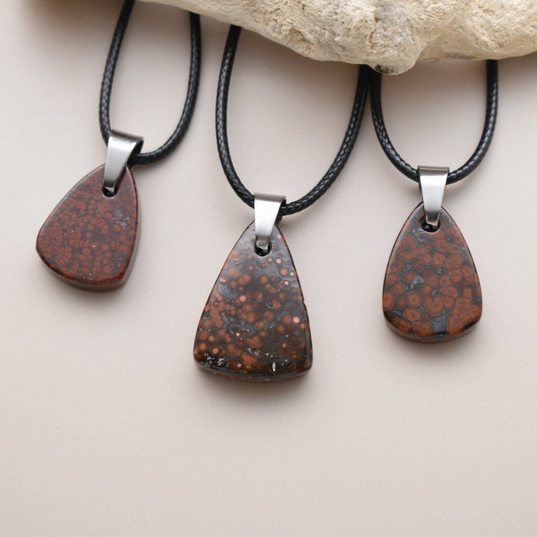 Three teardrop-shaped pendants on black cords with a stone background