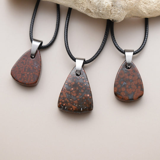 Three teardrop-shaped pendants on black cords with a stone background