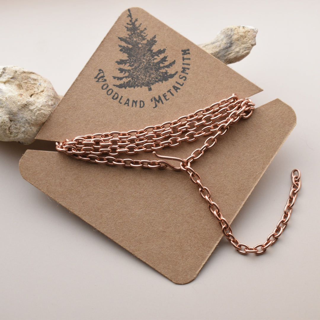 Rose gold chain on a wooden stand with 'Woodland Metalsmith' branding.