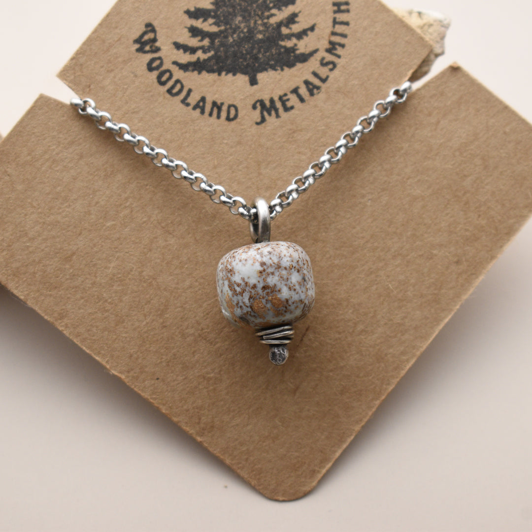 Necklace with a blue stone pendant on a 'Woodland Metalsmith' branded card.
