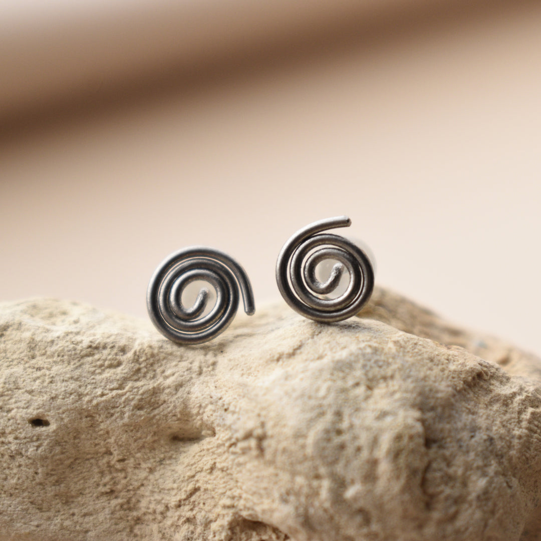 Silver spiral earrings on a textured beige surface