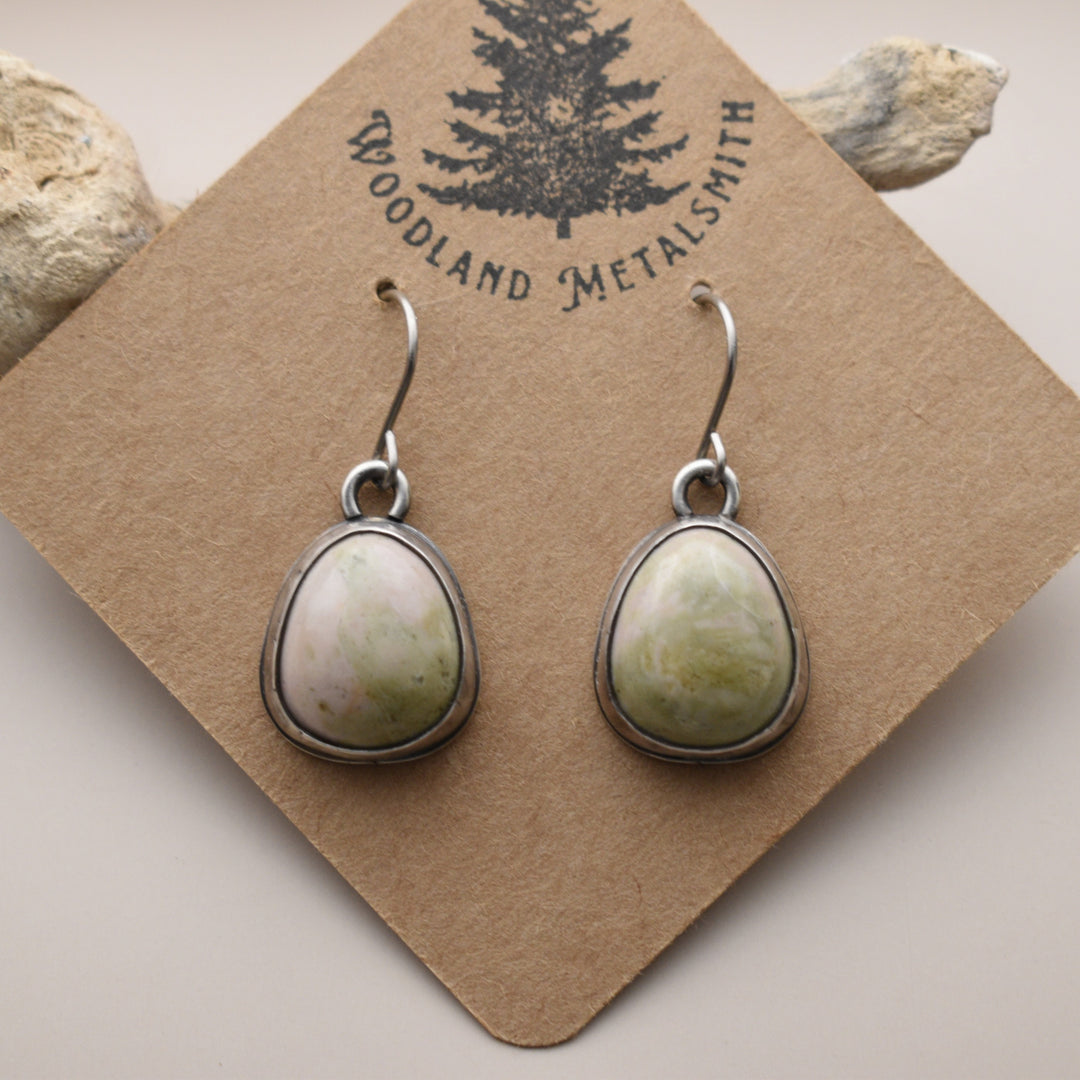 Teardrop-shaped earrings on a 'Woodland Metalsmith' branded card with rocks in the background.