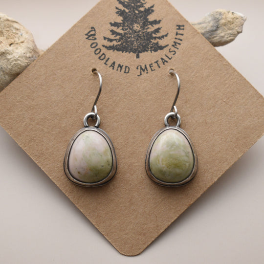 Teardrop-shaped earrings on a 'Woodland Metalsmith' branded card with rocks in the background.
