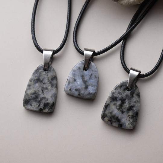 Three stone pendants on black cords with silver clasps on a light background