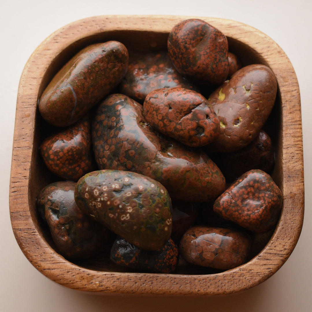 Wooden bowl filled with polished red jasper stones on a beige background